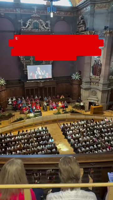 Clip filmed from the balcony of a hall, showing graduands holding flags, banners and wearing keffiyehs walk out of their graduating ceremony