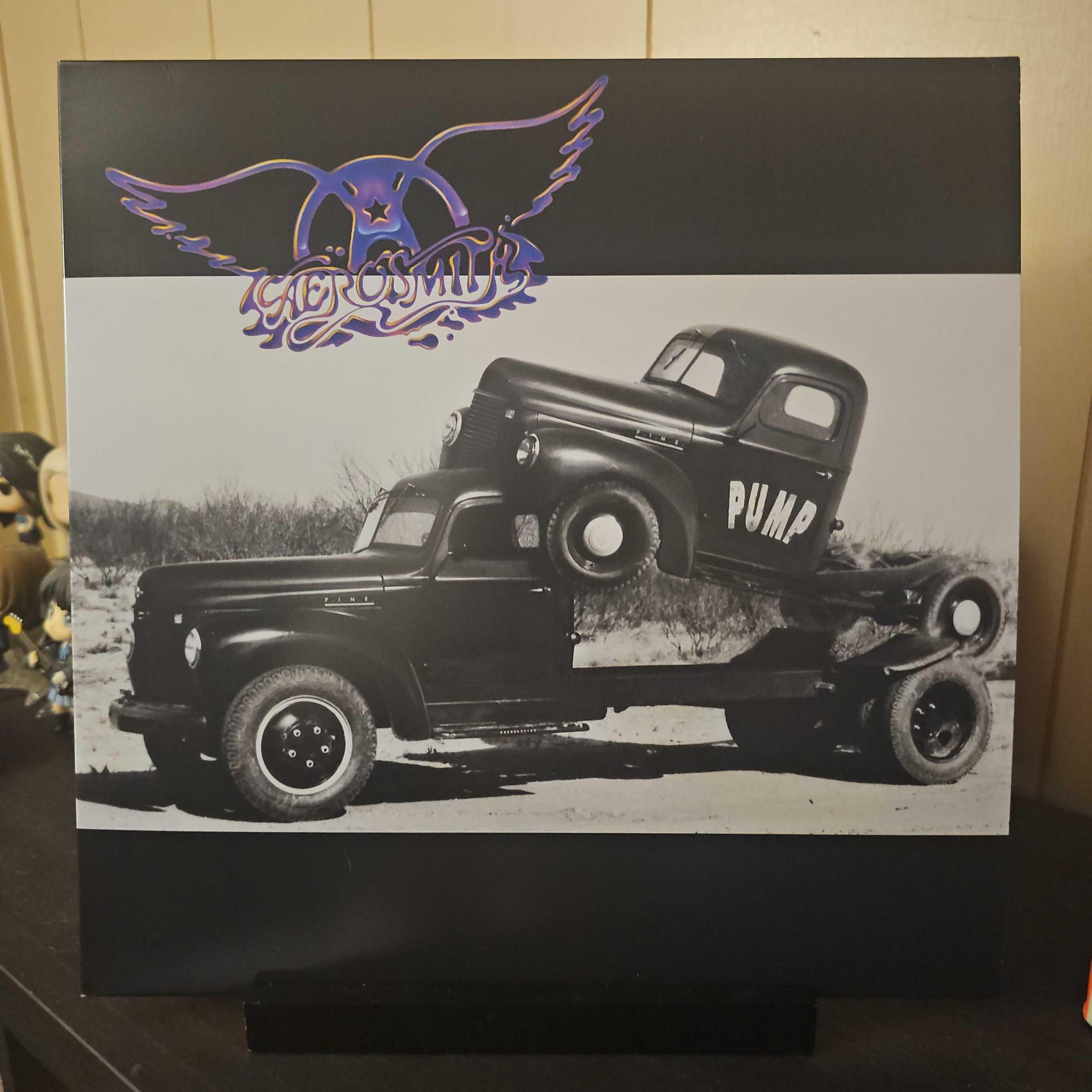 A vinyl record album outer sleeve is displayed. The front cover shows a small truck sitting on the back of a larger truck, but the front is resting on the top of the cabin. The smaller truck says "Pump" on the side.